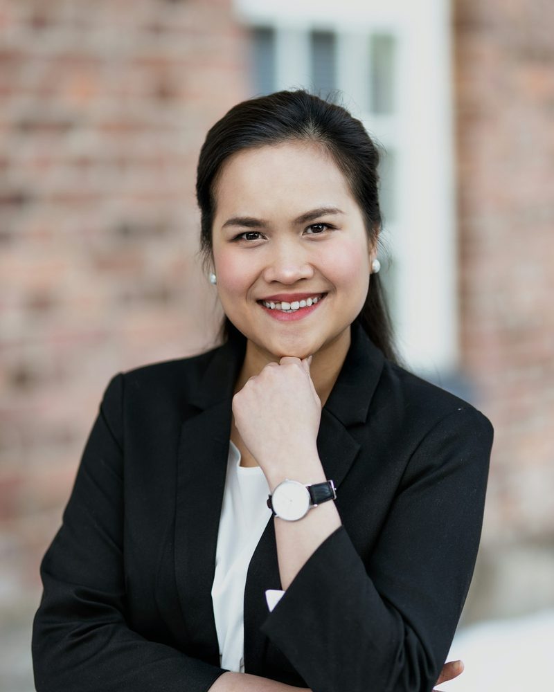 Portrait von Claudia Lindner mit zurückgebundenen dunklen Haaren, schwarzem Blazer und Armbanduhr, sie lächelt